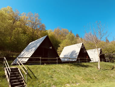 Mehrere A-förmige Zeltplatz-Hütten aus Holz auf einer grünen Wiese im Ferienzentrum Albert Schweitzer in Vöhl.