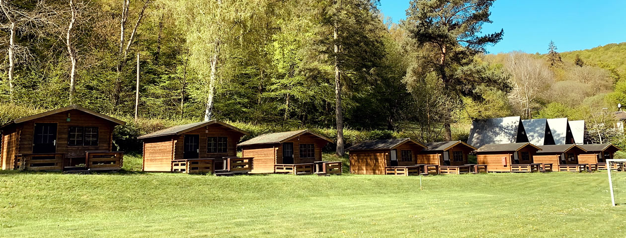Eine Reihe von kleinen Holzhäuschen auf einer grünen Wiese im Ferienzentrum Albert Schweitzer in Vöhl.