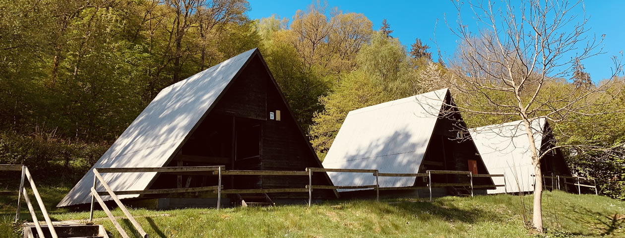 Drei A-förmige Zelthäuser aus Holz mit weißen Dächern auf einer grünen Wiese im Ferienzentrum Albert Schweitzer in Vöhl.
