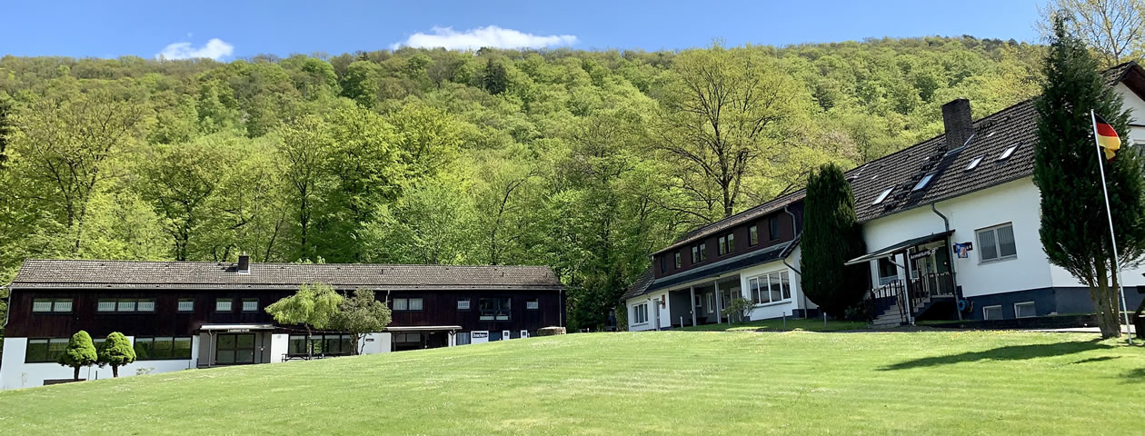 Der Außenbereich des Ferienzentrums Albert Schweitzer in Vöhl mit Gebäuden, Tischen und einem Wald im Hintergrund