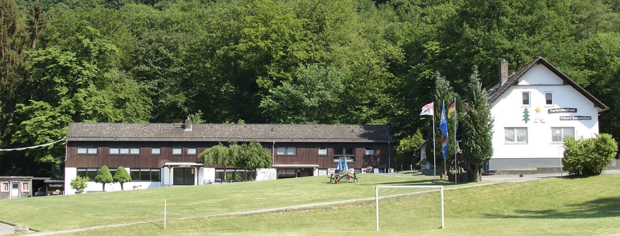 Der Außenbereich des Ferienzentrums Albert Schweitzer in Vöhl mit Gebäuden, Tischen und einem Wald im Hintergrund