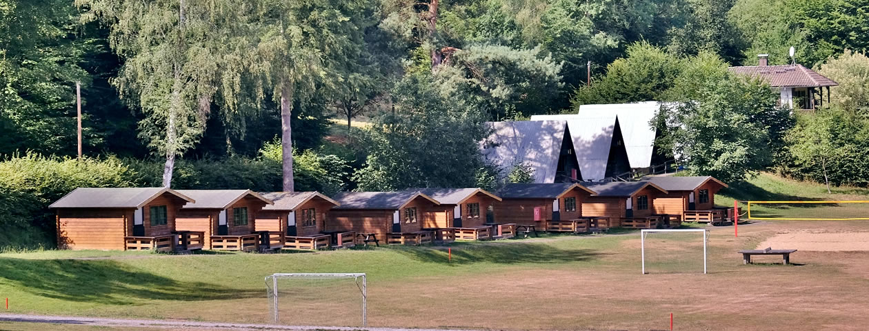 Eine Reihe von kleinen Holzhäuschen auf einer grünen Wiese im Ferienzentrum Albert Schweitzer in Vöhl.