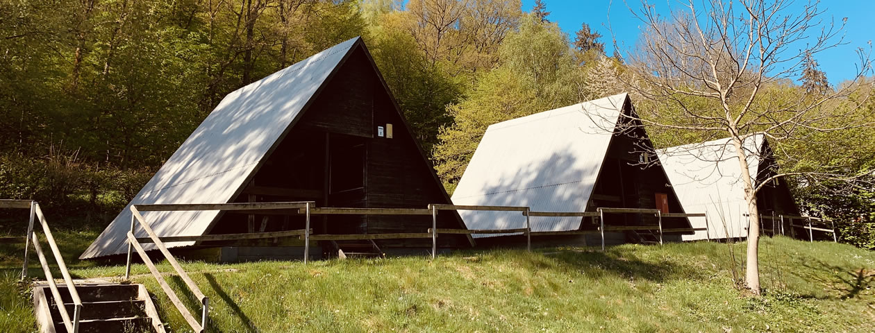 Drei A-förmige Zelthäuser aus Holz mit weißen Dächern auf einer grünen Wiese im Ferienzentrum Albert Schweitzer in Vöhl.